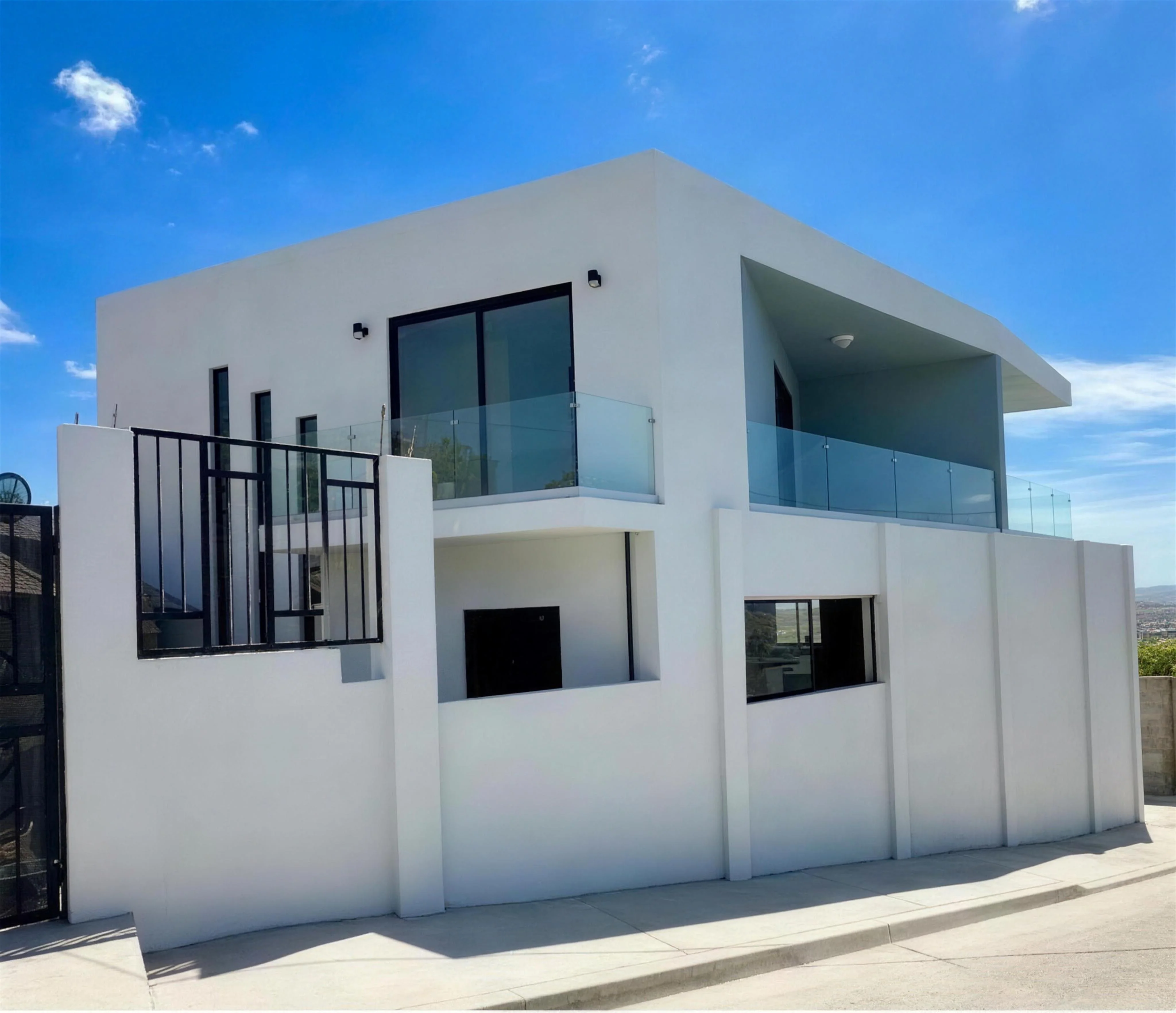 Casa Terrazas: residencia blanca de dos niveles terminada, con terrazas de barandal de cristal sobre la ladera